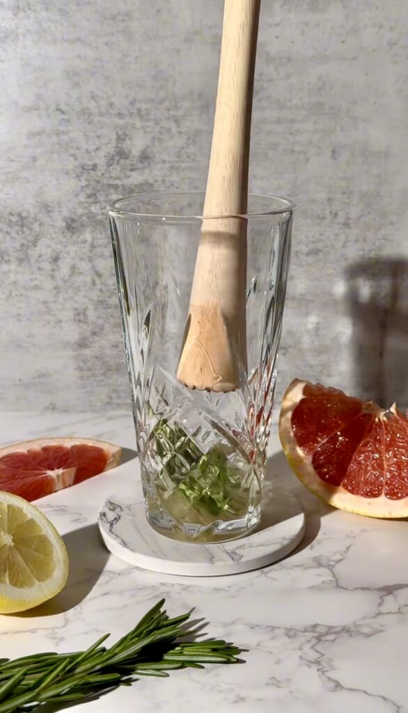 Muddling rosemary, cane sugar, and gin to form the base of the Grapefruit Rosemary Spritz cocktail